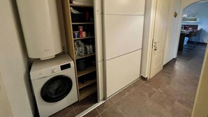 A laundry area with a washing machine, a storage closet, and a kitchen area visible in the background.