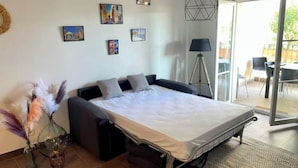 A modern bedroom with a bed, a side table, and a lamp. There are paintings on the wall and a window with a view of the outside.