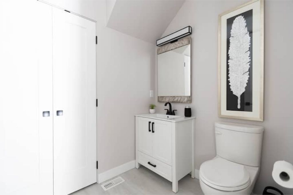 A modern bathroom with a white vanity, a toilet, and a framed leaf artwork on the wall.