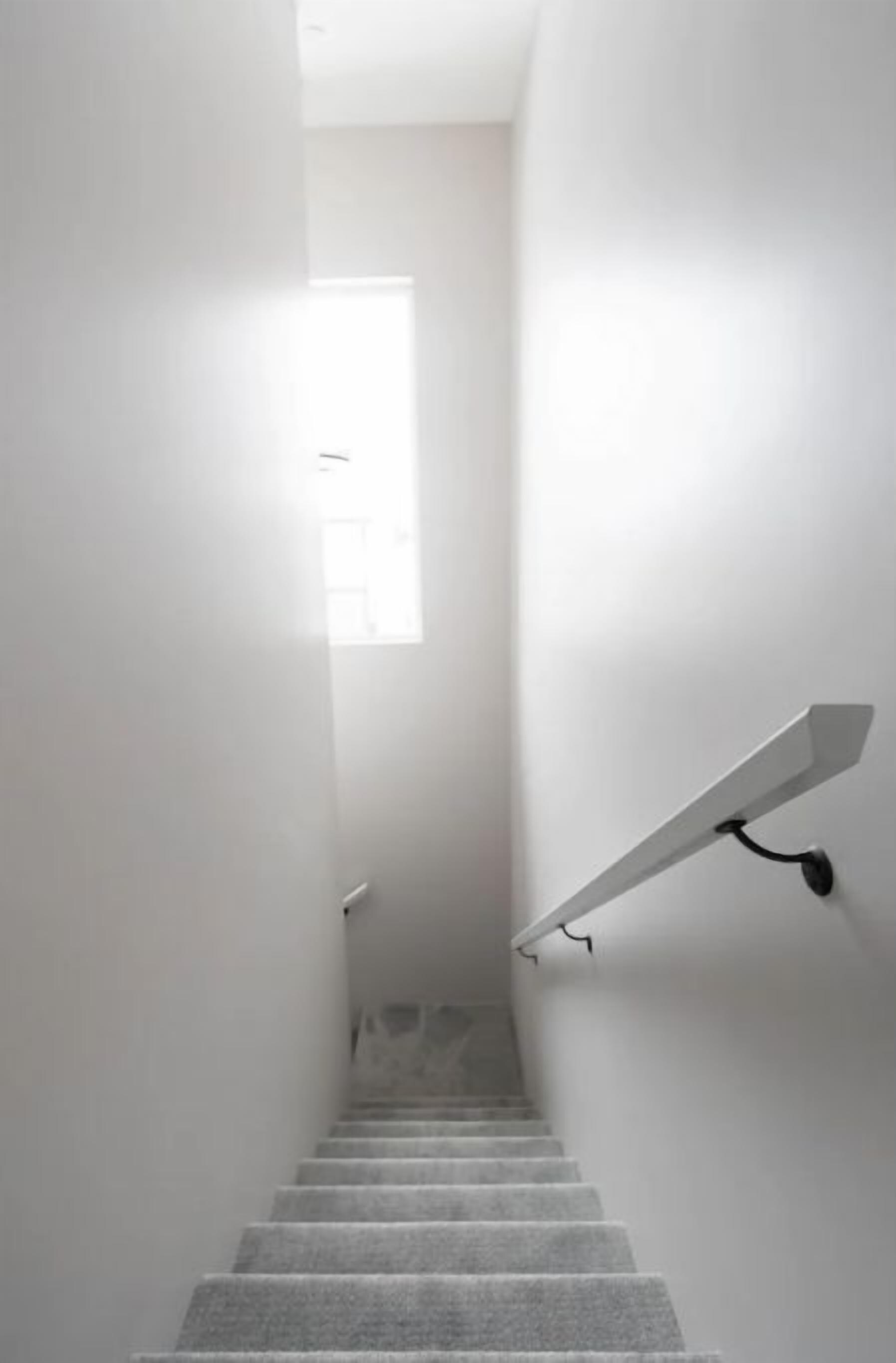 Un escalier étroit et bien éclairé, avec un luminaire sur le côté droit et une fenêtre en haut.