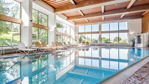 A large indoor swimming pool with clear blue water, wooden ceiling beams, and large windows offering views of the outdoors. - Hotel Inntaler Hof (Telfs)