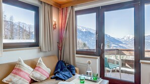 A cozy room with a bed, a table with glasses and a book, and a balcony with a view of mountains. - Hotel Inntaler Hof (Telfs)