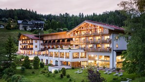 A multi-story hotel with balconies and large windows, surrounded by a well-maintained lawn and trees. - Hotel Inntaler Hof (Telfs)
