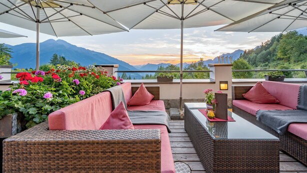 An outdoor seating area with wicker furniture, a table, and umbrellas providing shade. - Hotel Inntaler Hof (Telfs)