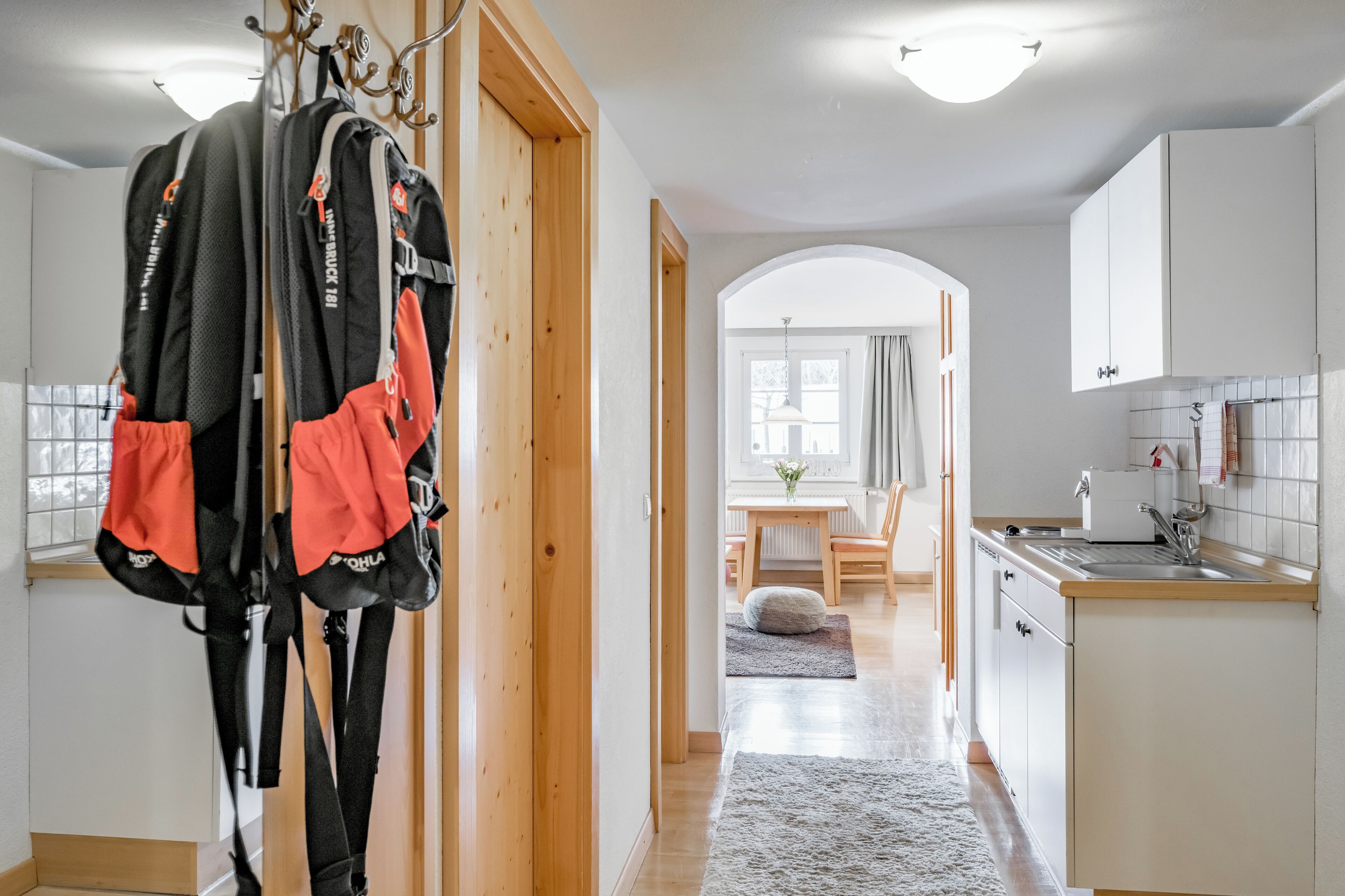 Una cocina moderna con armarios blancos, encimera de madera y un lavabo. Un pasillo conduce a un comedor con mesa y sillas.