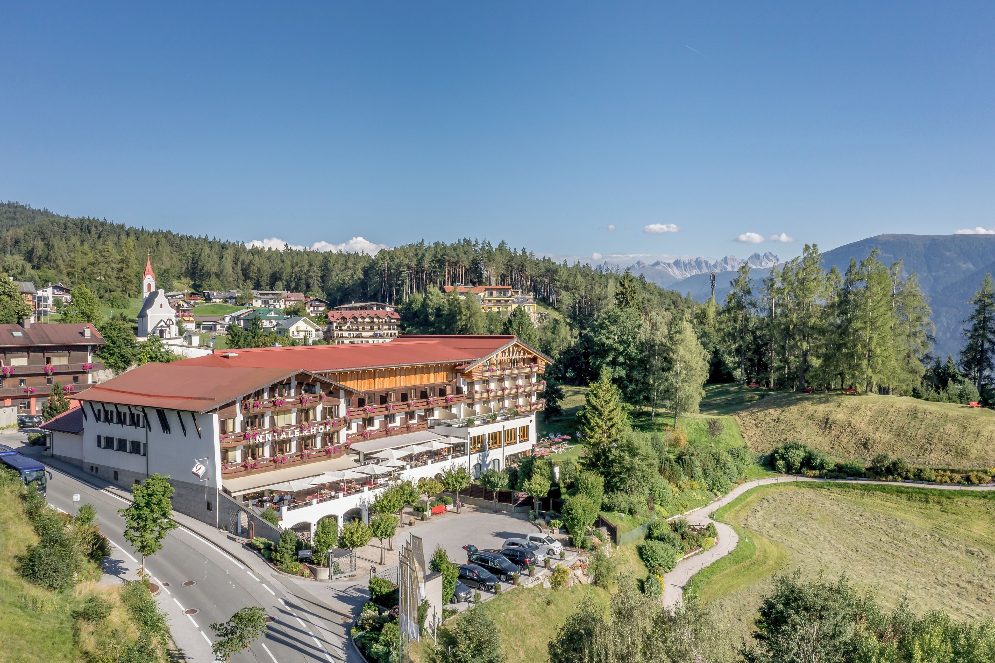 A hotel with a red roof, multiple balconies, and a view of mountains in the background.