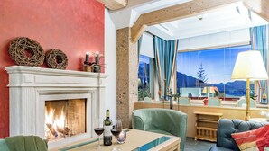 A cozy room with a fireplace, a table with wine glasses, a sofa, and a large window with a mountain view. - Hotel Inntaler Hof (Telfs)