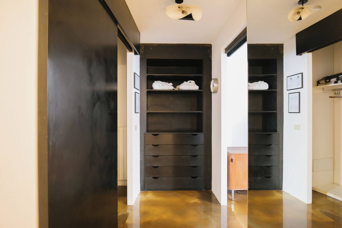 A hallway with a polished floor, a black storage unit with shelves, and a small wooden cabinet.