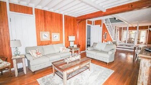 A spacious living room with wooden floors, two white sofas, a coffee table, and a staircase leading to another level. - Historic Lake Front Home (Auburn)