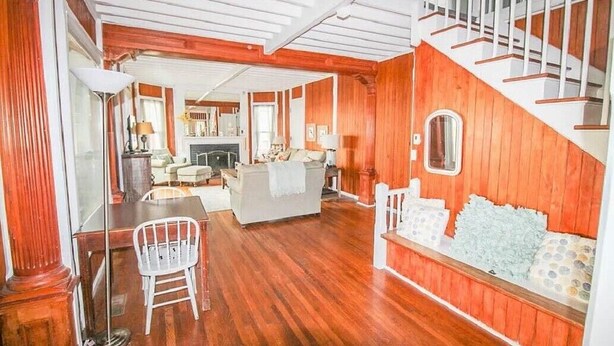 A spacious living room with a fireplace, a dining area with a table and chairs, and a staircase with a railing. - Historic Lake Front Home (Auburn)
