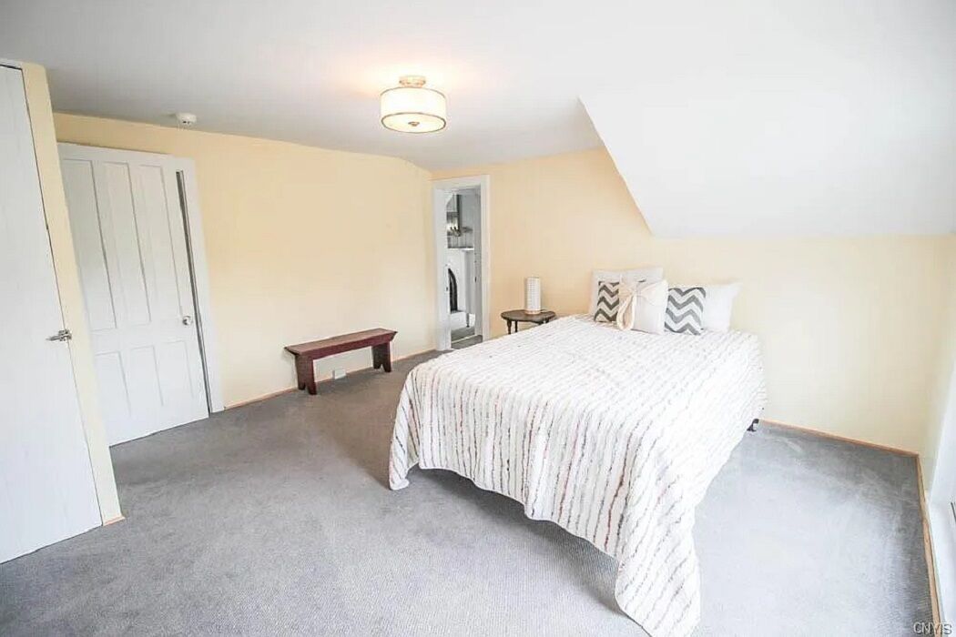 Een slaapkamer met een bed, een bankje, een nachtkastje en een deur.