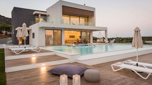 Een modern huis met een zwembad, terras en een balkon met uitzicht op het zwembad.