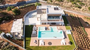 Een modern huis met twee verdiepingen, een groot zwembad, een overdekt terras en een verzorgd gazon.