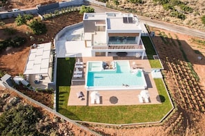 A modern two-story house with a large swimming pool, a covered patio, and a well-maintained lawn.