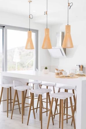 A modern kitchen with white countertops, wooden stools, and pendant lights.