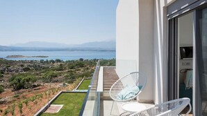 Een balkon met uitzicht op zee en bergen, witte stoelen en een glazen deur.