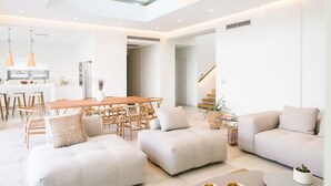Een moderne woonkamer met een hoge plafond, een eethoek met houten meubels, en een neutraal kleurenpalet.