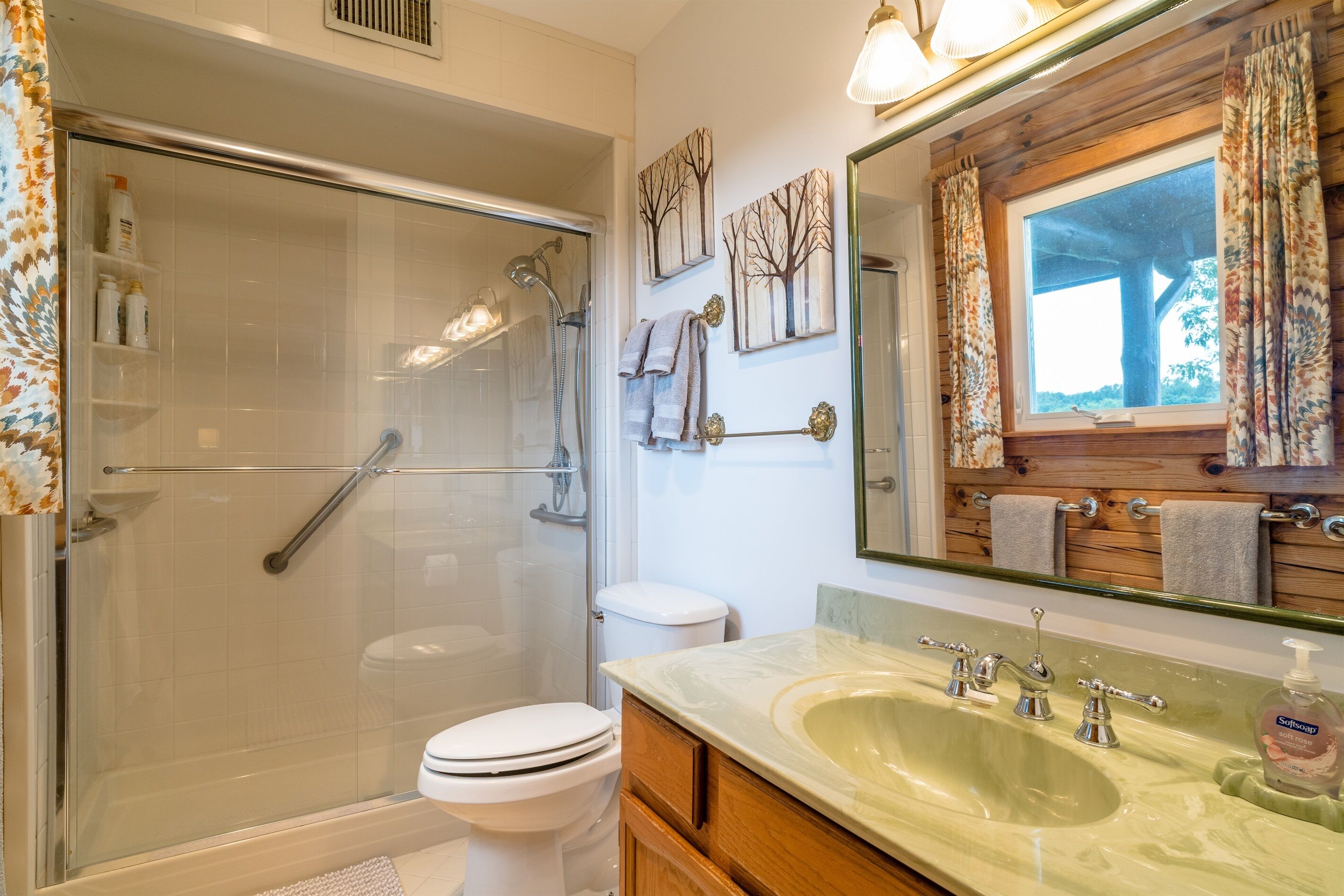 A bathroom with a glass-enclosed shower, a white toilet, a sink with a marble countertop, and a mirror with a wooden frame.