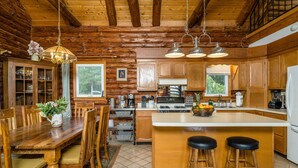 Une cuisine de style rustique, avec des éléments en bois, comprenant un îlot central, des tabourets de bar et un coin repas avec des chaises et une table en bois.