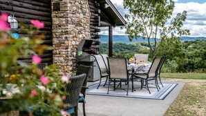 Une terrasse avec un mur en pierre, un barbecue et une table avec des chaises.