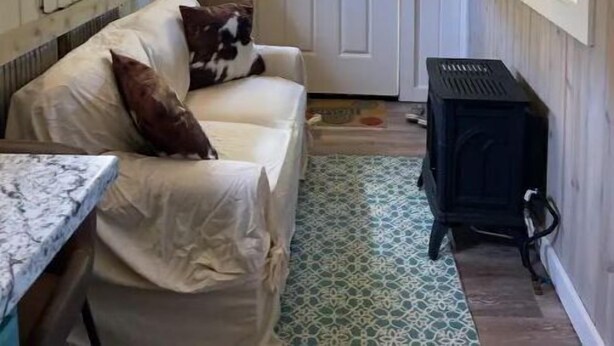 Um quarto aconchegante com teto de madeira, porta branca, sofá com manta, mesa pequena, aquecedor e TV fixada na parede.