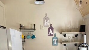 Cozinha compacta com geladeira, pia e armários. Há canecas penduradas e um objeto decorativo na parede com letras.