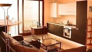 Een knus woongedeelte met een bank, een klein tafeltje, een kitchenette en een balkon.