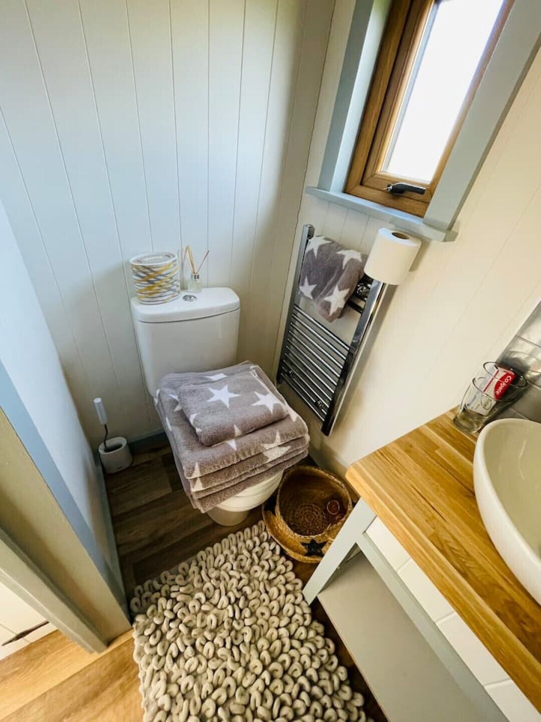 A compact bathroom with a toilet, a towel rack with a star-patterned towel, a small sink, and a window above the toilet.