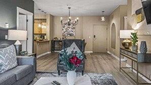 Ein modernes Wohnzimmer mit einem grauen Sofa, einem Couchtisch, einem dekorativen Sessel mit Vase und einem Essbereich im Hintergrund.