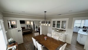 A spacious dining area with a wooden table and white upholstered chairs, a kitchen with white cabinetry and a built-in oven, and a living area with a sofa and a television. - Craftsman house 500 yards to beach and short walk to many restaurants (Long Beach)