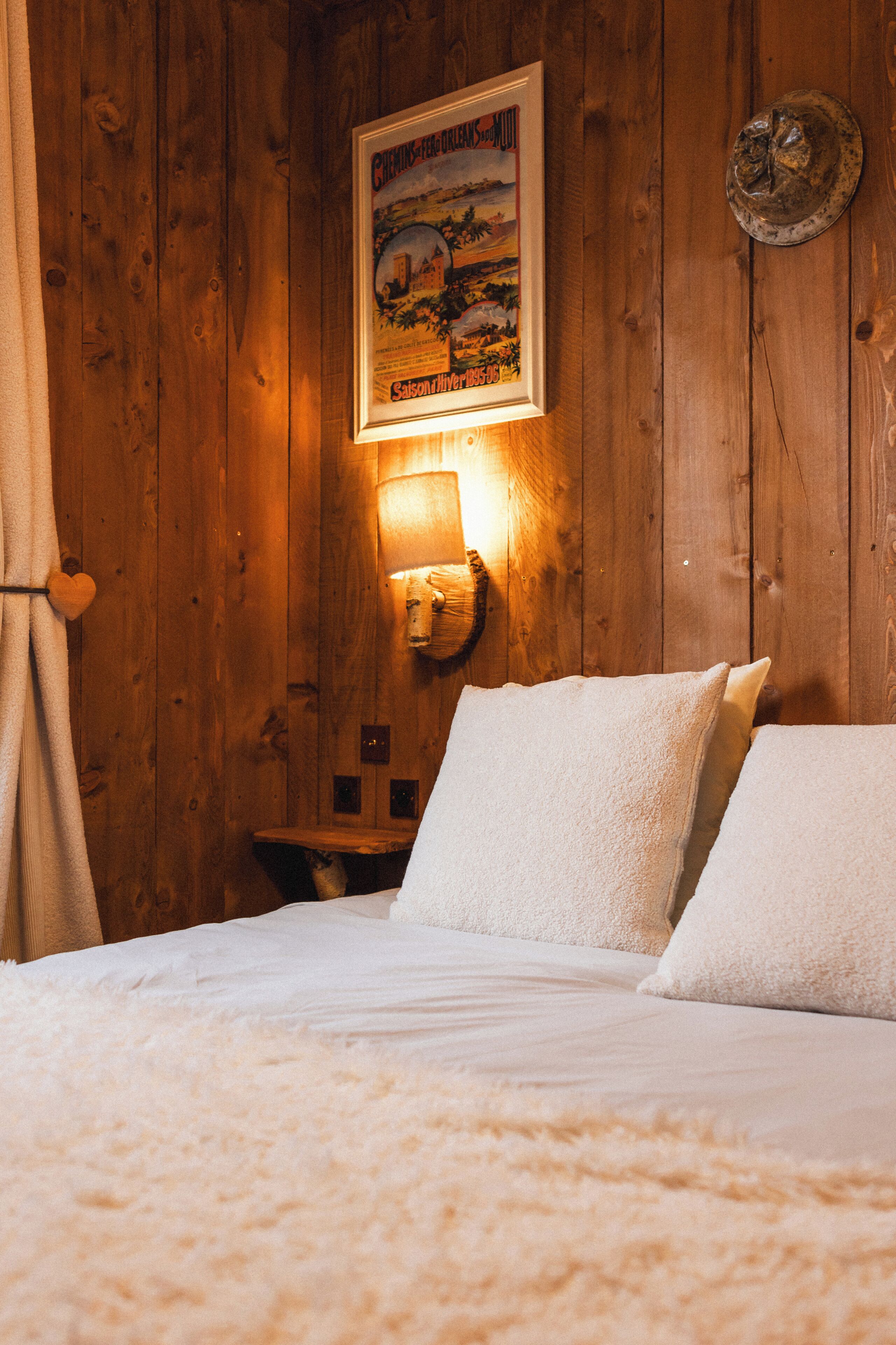 A wooden room with a bed, a wall-mounted lamp, and a framed picture.