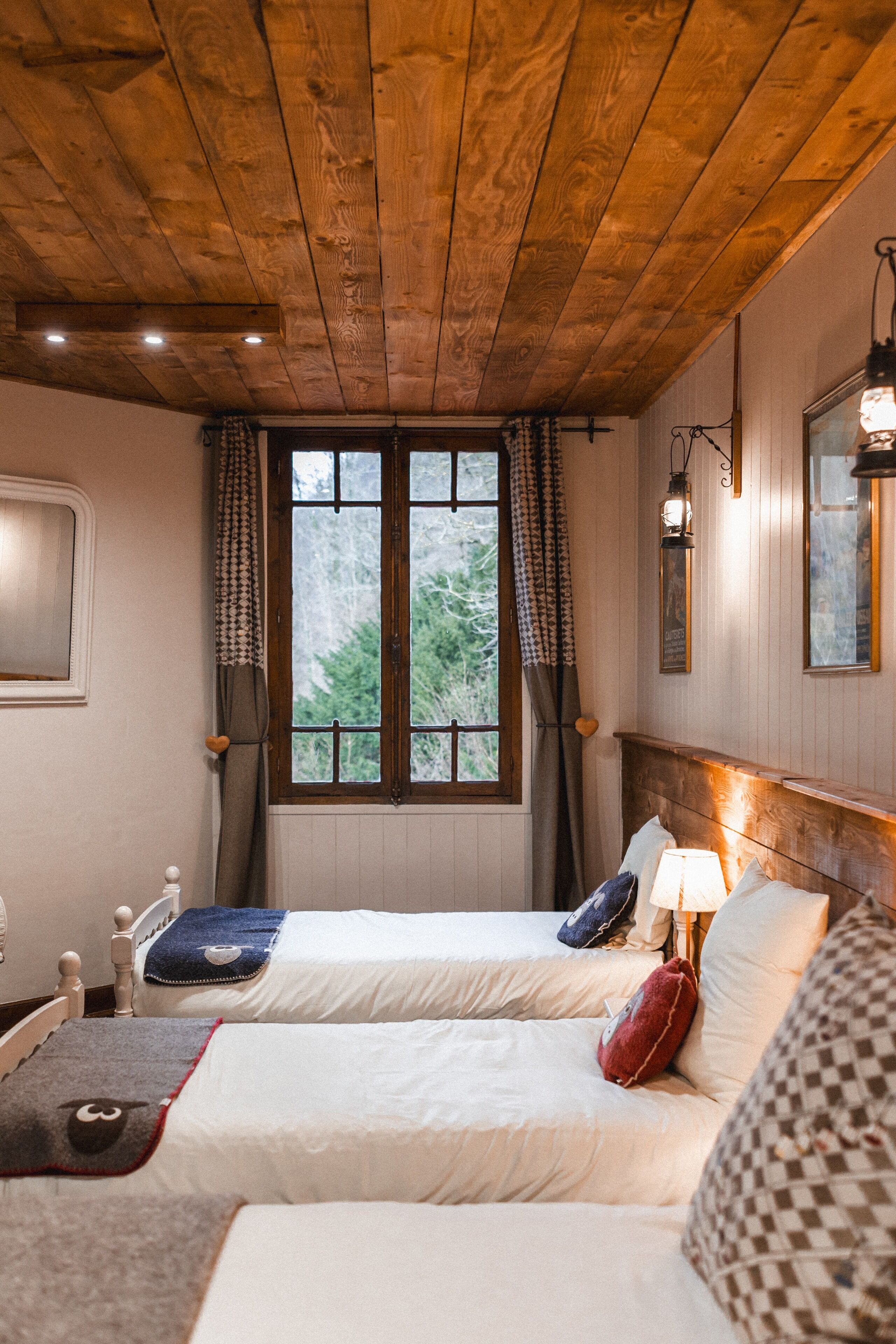 Habitación con dos camas, techo de madera, ventana con cortinas y una lámpara.