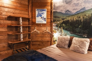 Acogedora habitación de cabaña de madera con cama, un cartel de un paisaje montañoso y un perchero.