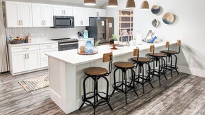 A modern kitchen with white cabinets, a central island with stools, a microwave, and a refrigerator.