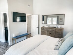 A bedroom with a bed, a bench, a dresser, a mirror, and a television.