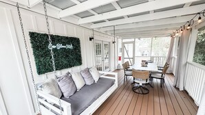 A covered porch with a swing seat, a dining table with chairs, and a hanging light fixture.