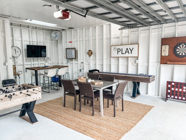 A room with a foosball table, a dartboard, and a table tennis table.