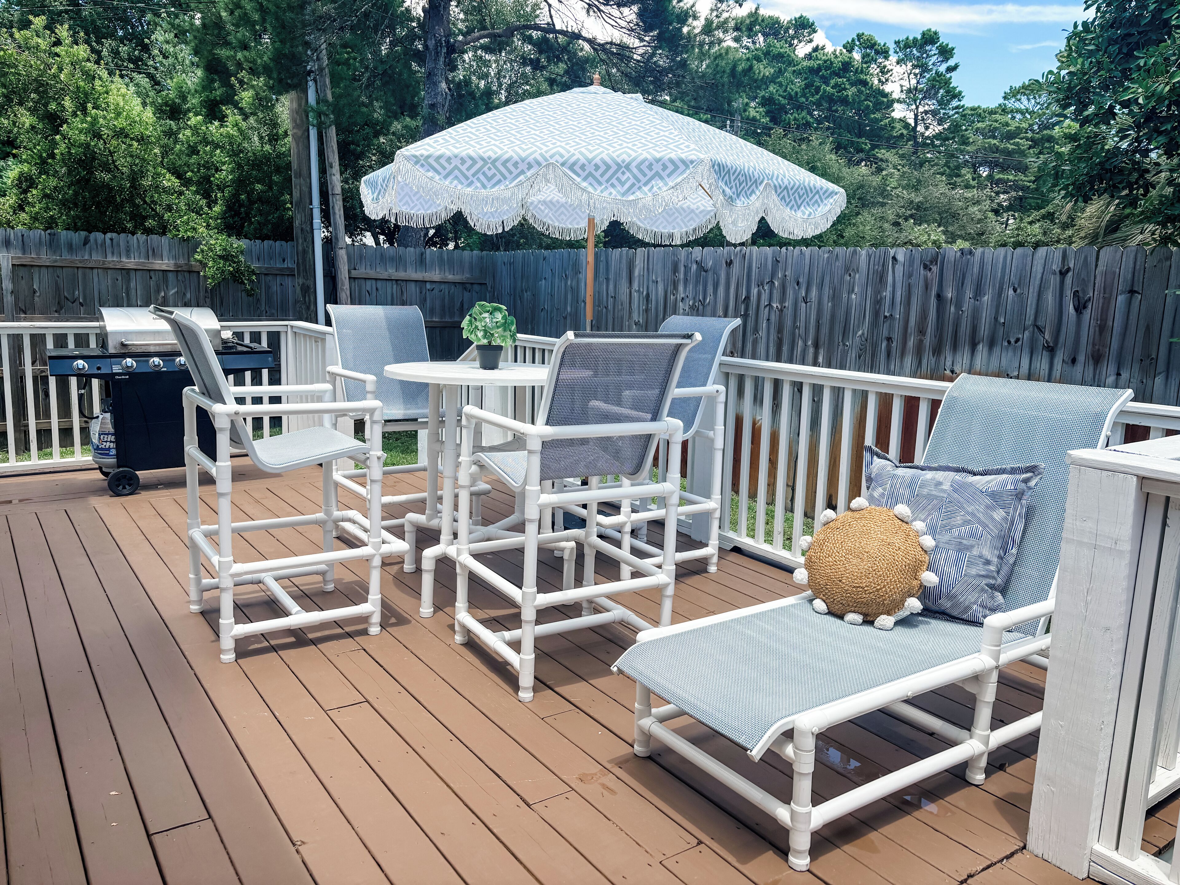 A deck with white furniture, including chairs and a table, and a grill.