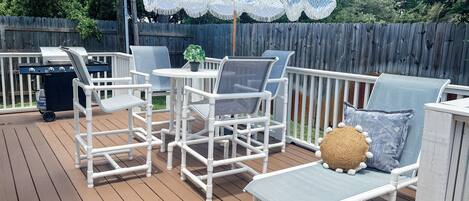 A deck with white furniture, including chairs and a table, and a grill.