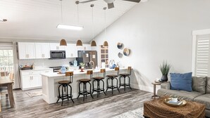 A modern kitchen with white cabinets, a central island with stools, a ceiling fan, and a dining area with a wooden table and chairs.