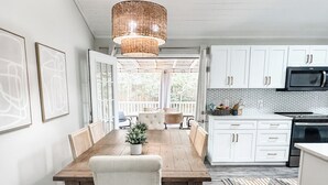 A modern kitchen with white cabinets, a dining area with a wooden table and bench, and a hanging light fixture.