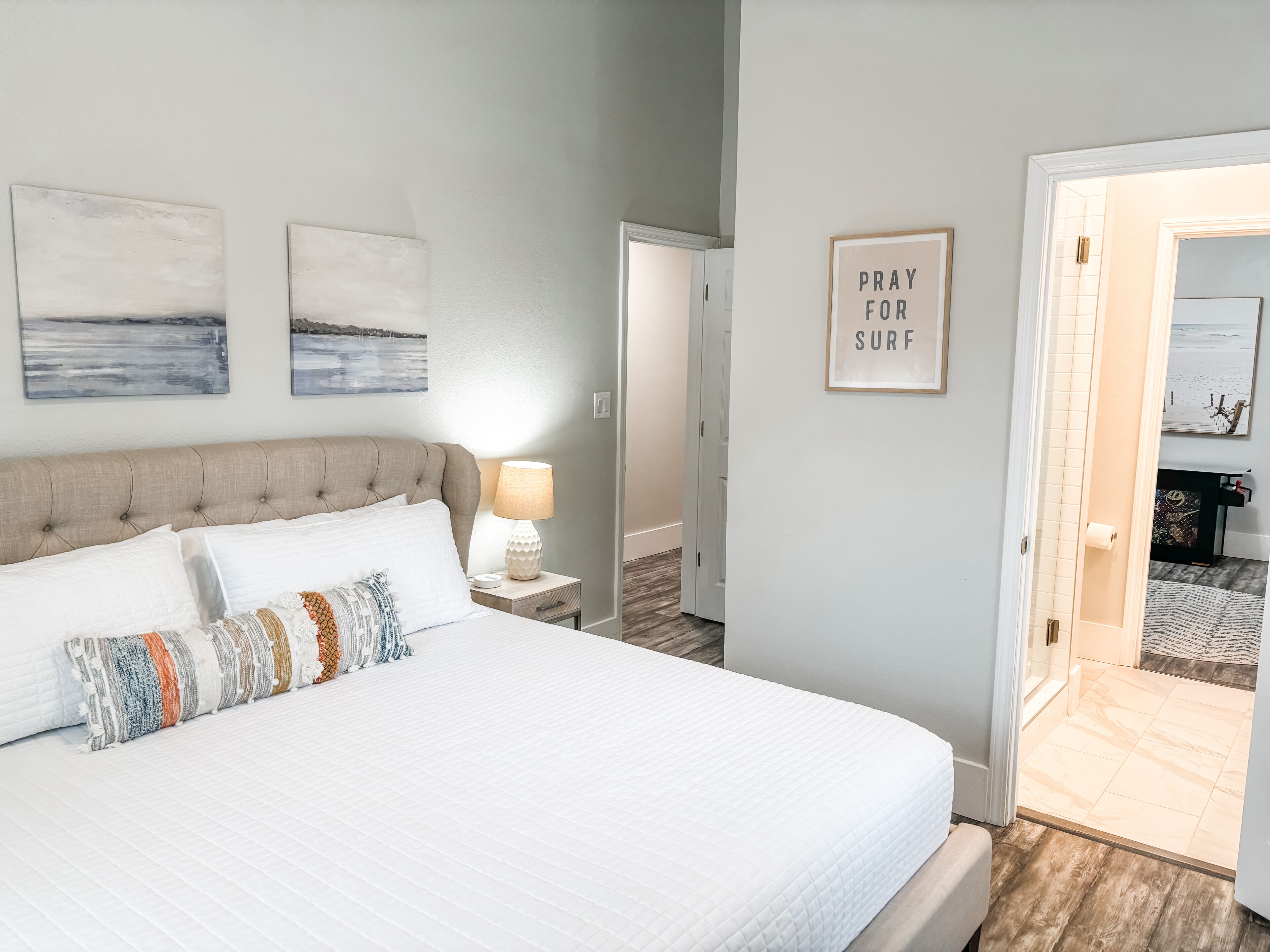 A bedroom with a large bed, a nightstand with a lamp, and two wall-mounted paintings.