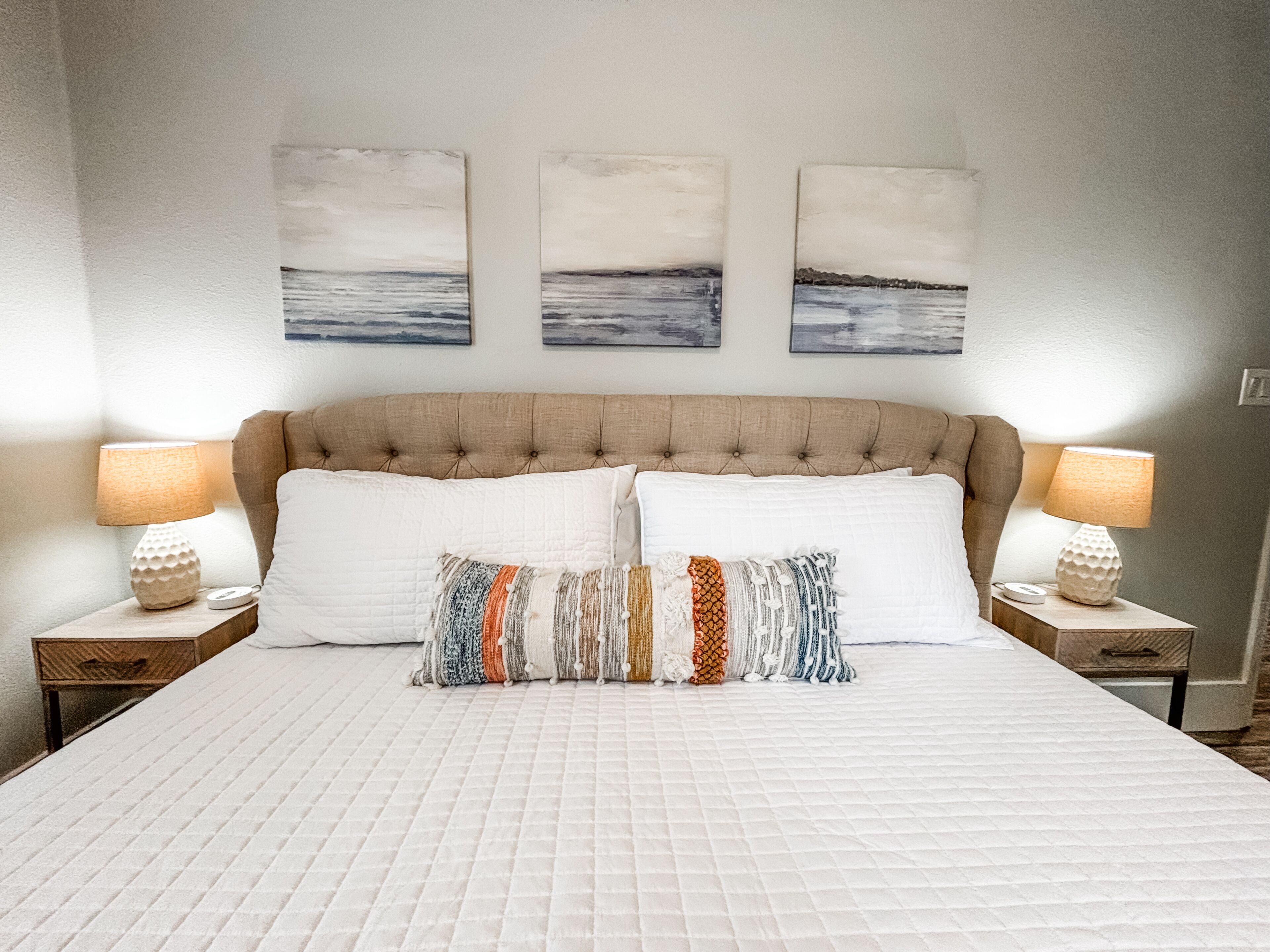 Ein Schlafzimmer mit einem großen Bett, zwei Nachttischen und drei Wandbildern.