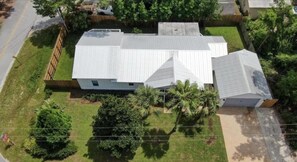 A two-story house with a metal roof, surrounded by a fenced yard and palm trees.