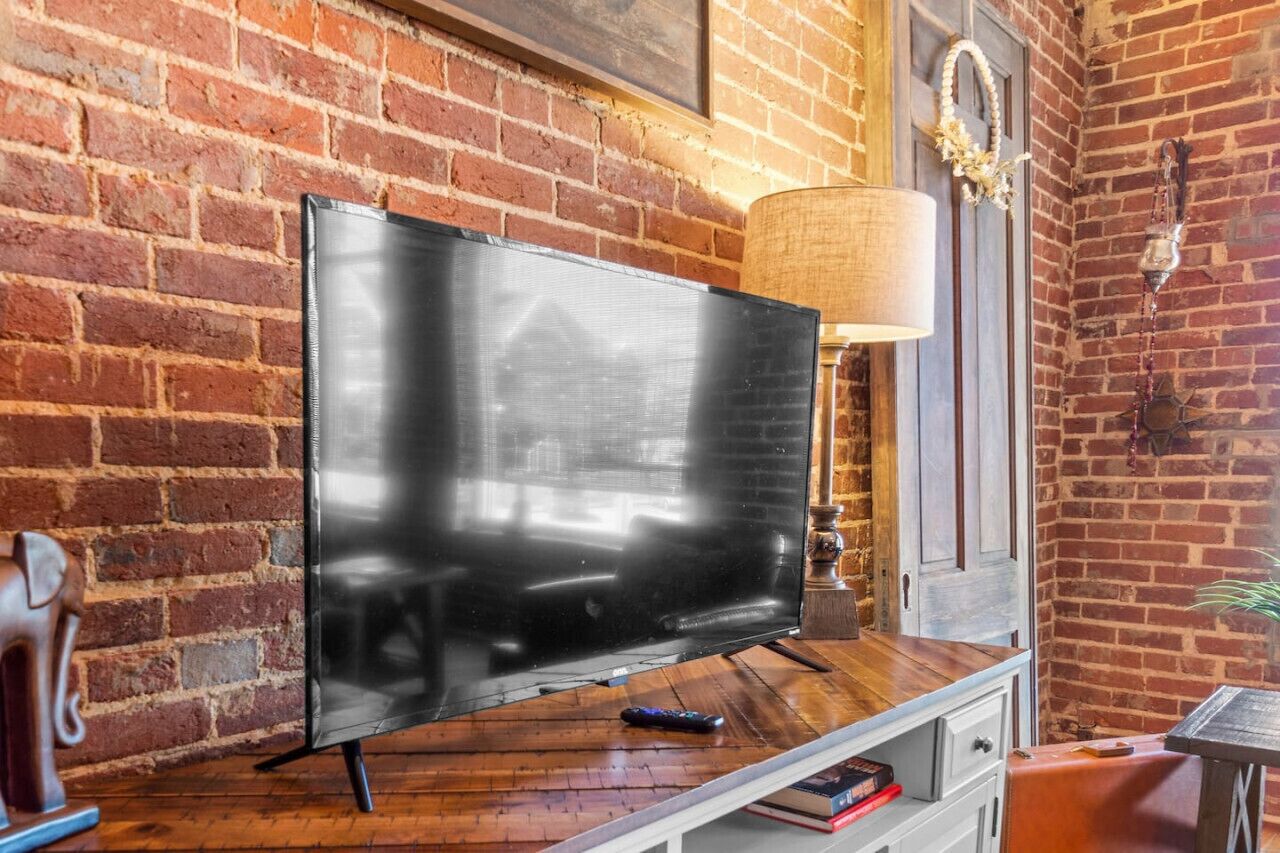 Un televisor de pantalla plana sobre un atril de madera en una habitación con paredes de ladrillo visto y suelo de madera.