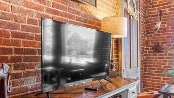 Un televisor de pantalla plana sobre un atril de madera en una habitación con paredes de ladrillo visto y suelo de madera.