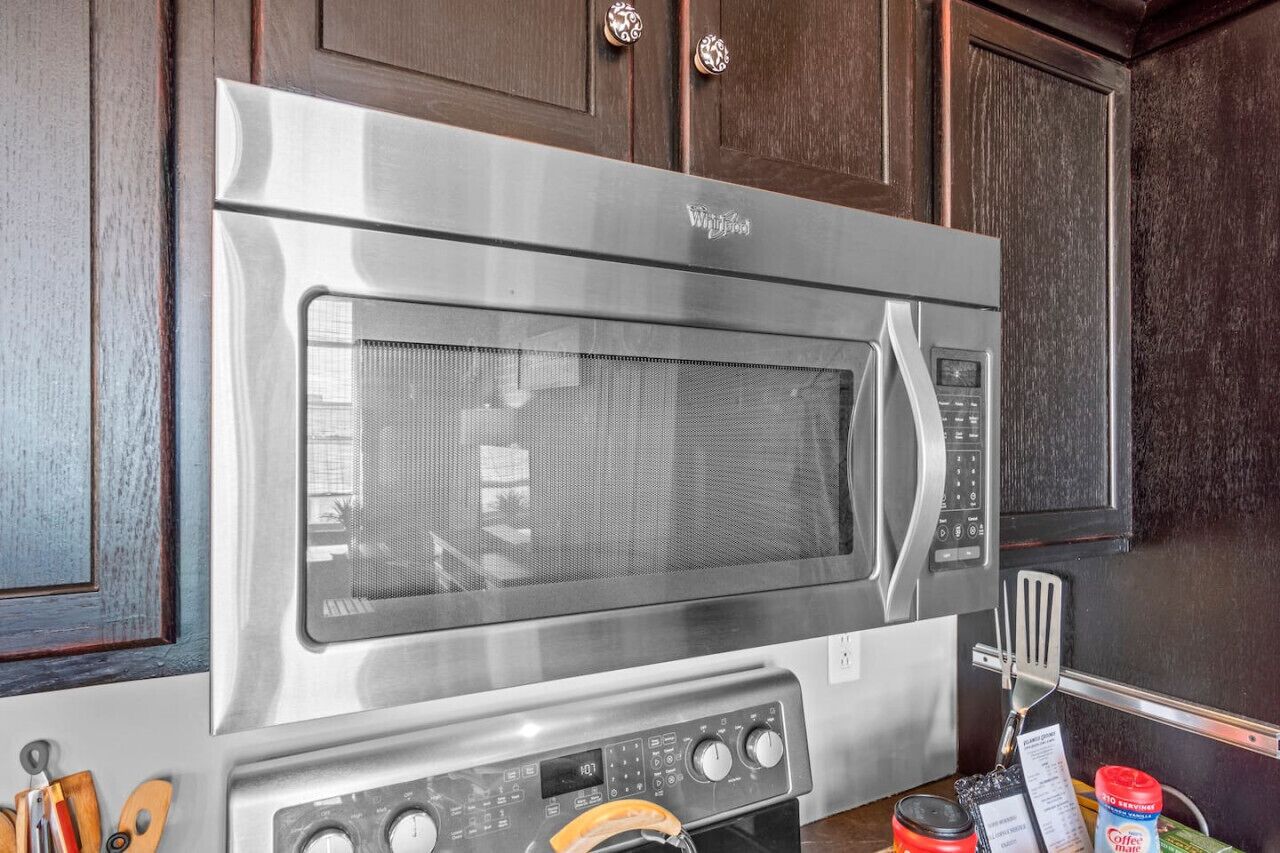A stainless steel microwave oven with a digital display and control panel, mounted on a wooden cabinet.
