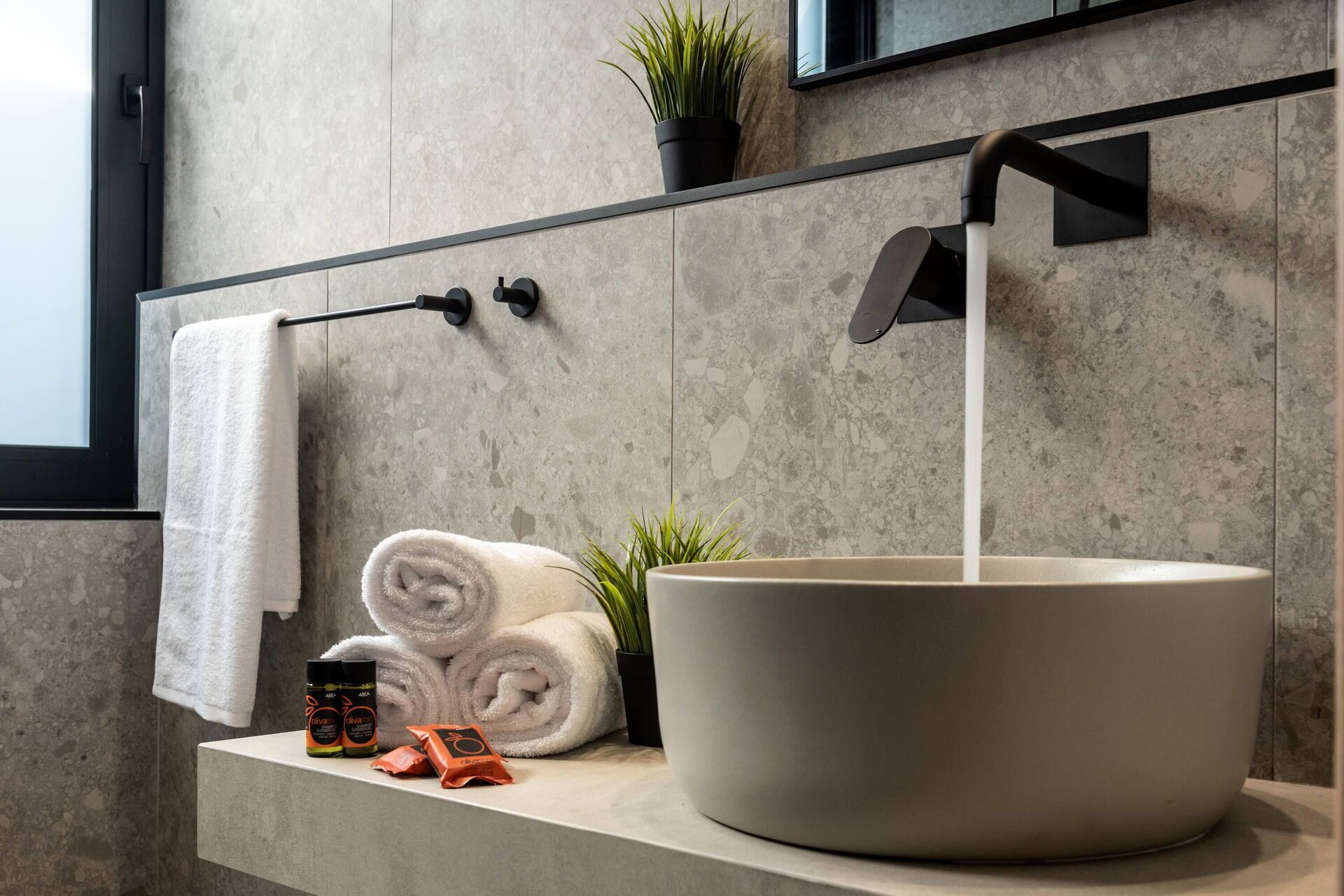 A bathroom with a large vessel sink, a towel rack, a potted plant, and toiletries on the counter.