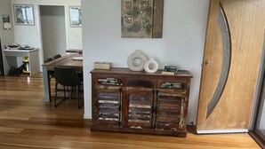 A dining area with a wooden table and chairs, a decorative cabinet with books and vases, and a door with a unique design. - Recovery On Discovery Holiday House (Agnes Water)