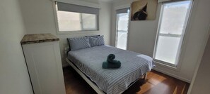 A bedroom with a bed, two windows, and a wooden floor. - Recovery On Discovery Holiday House (Agnes Water)